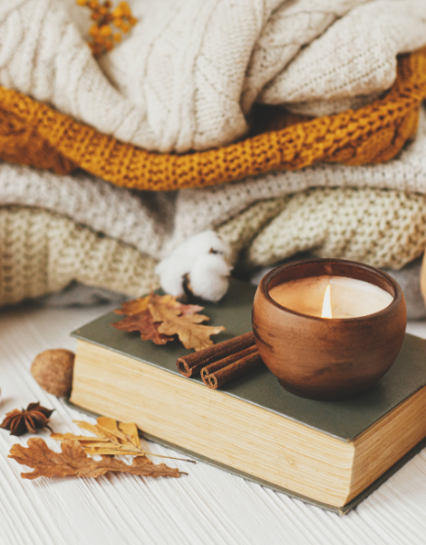 Image. Cosy Home Decor Essentials. Throw blankets. Scented candle. A book. And autumn leaves.